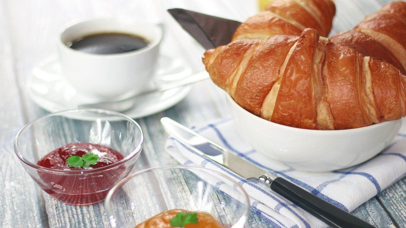 Breakfast table with a cup of coffee, a croissant and small bowls of jam