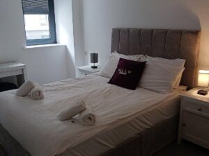 Neatly made bed with white linens and a lit bedside lamp in a calm bedroom