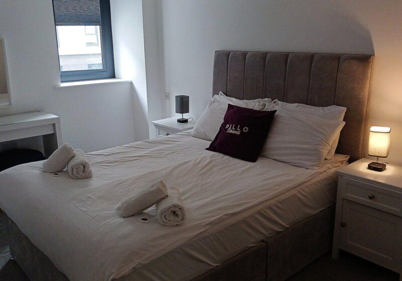 Neatly made bed with white linens and a lit bedside lamp in a calm bedroom