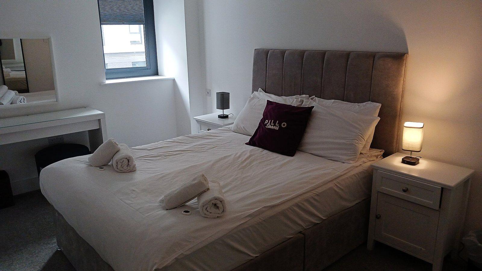 Neatly made bed with white linens and a lit bedside lamp in a calm bedroom