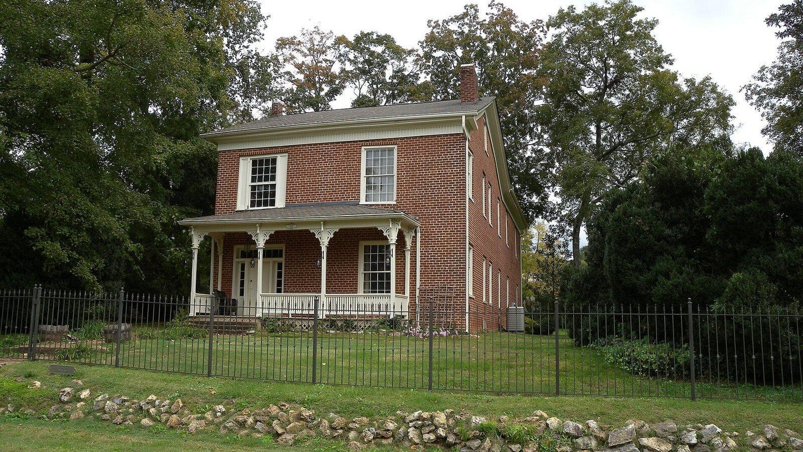 Historic red brick house with a front porch, garden fence and mature trees