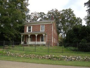 Historic red brick house with a front porch, garden fence and mature trees