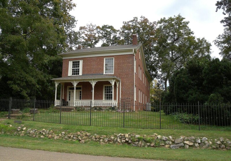 Historic red brick house with a front porch, garden fence and mature trees