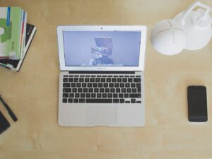 Top-down view of an open laptop on a light wooden desk with a phone and notebooks