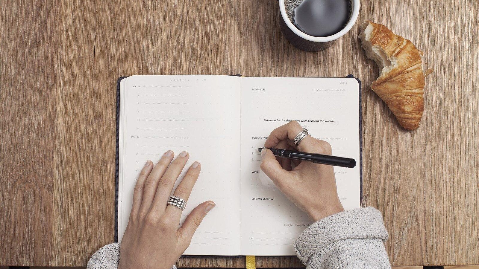 Person writing meeting notes in an open notebook next to a cup of coffee