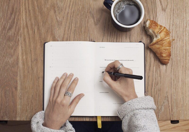 Person writing meeting notes in an open notebook next to a cup of coffee