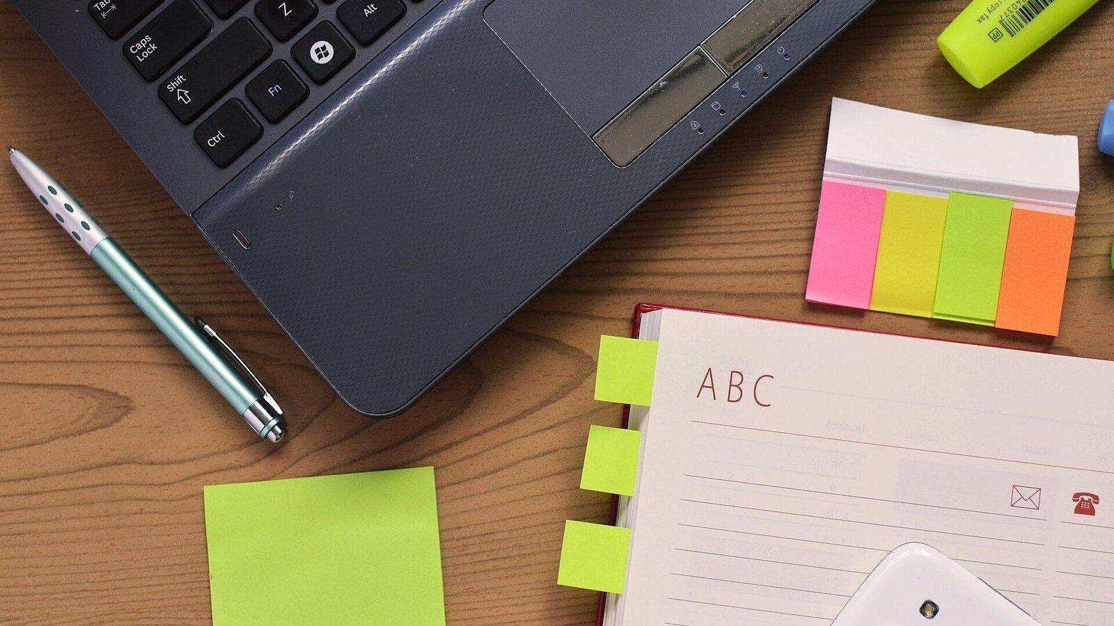 Desk with a laptop, notebook, pen and colorful sticky notes for business planning